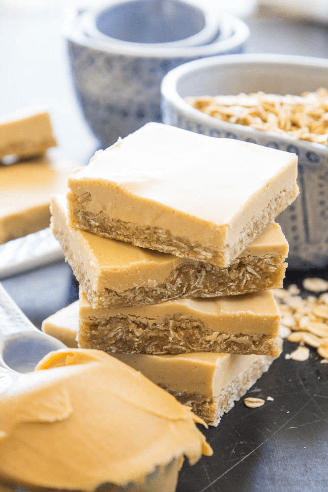 stack of Peanut Butter Oatmeal squares with spoonful of peanut butter and a bowl of oats