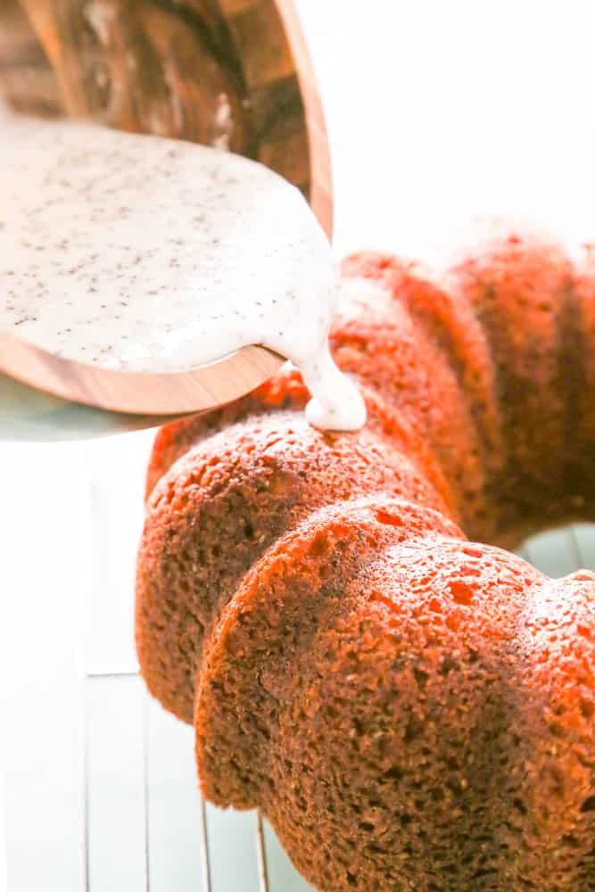 glaze being poured from a metal bowl onto Poppy Seed bundt cake on wire rack