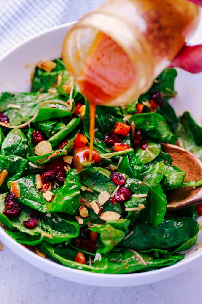 copycat dorothy lynch dressing in mason jar being poured onto almond cranberry spinach salad in a white bowl