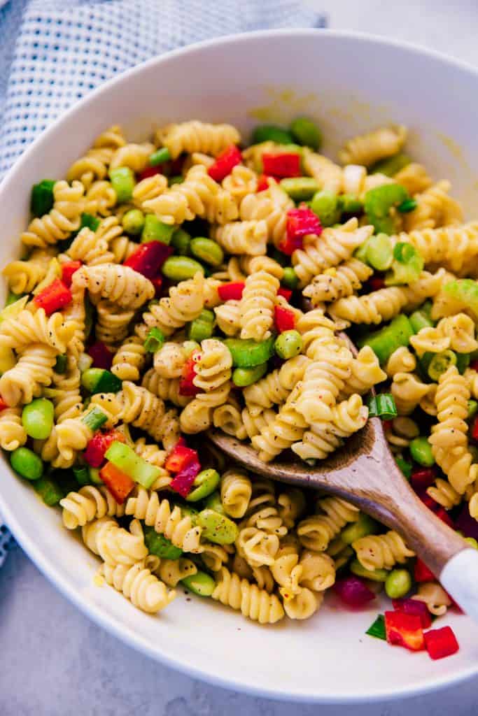mustard ginger pasta salad in a white serving bowl with wooden serving spoon