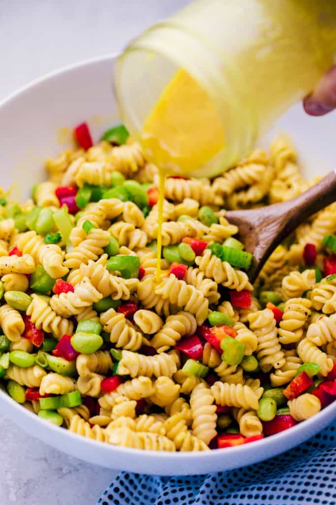mustard ginger dressing being poured from mason jar onto rotoni pasta salad with peppers and soybeans