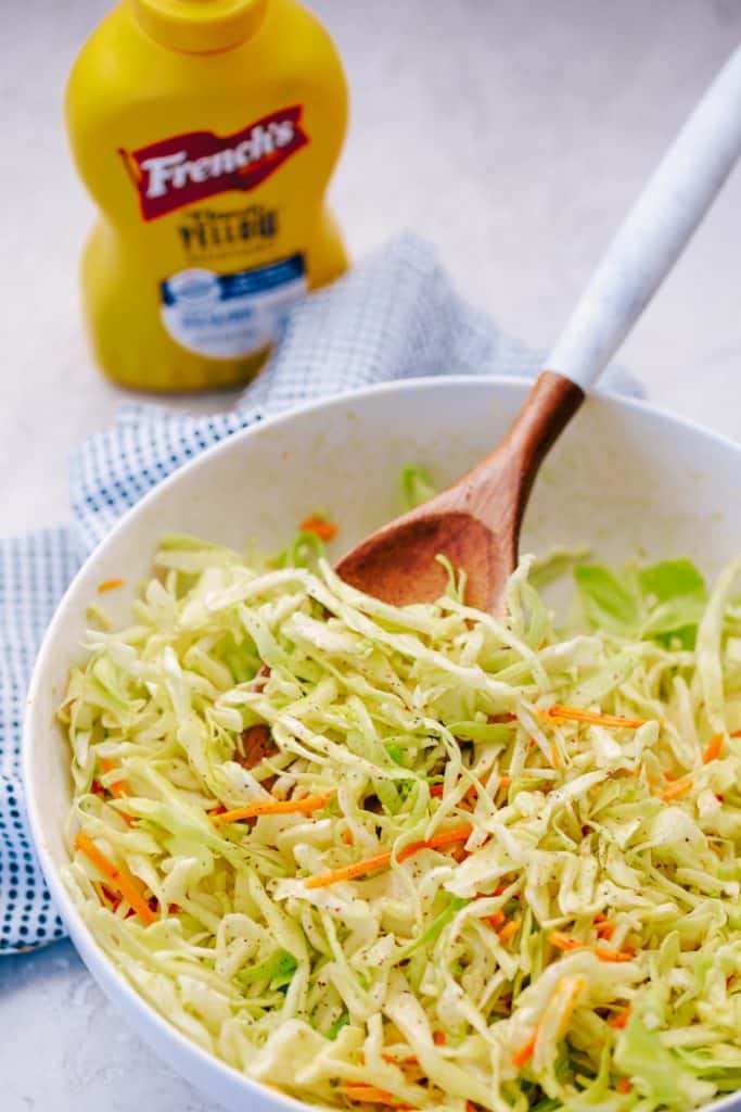 tangy coleslaw in a white bowl next to mustard bottle