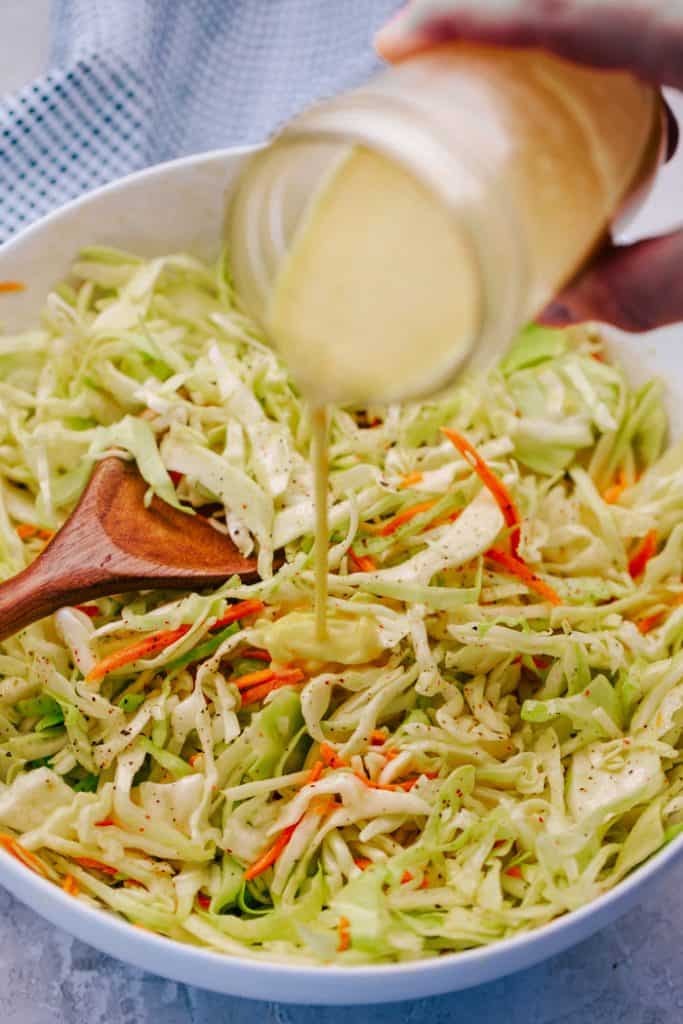 tangy dressing being poured from mason jar on sliced cabbage coleslaw in a white bowl