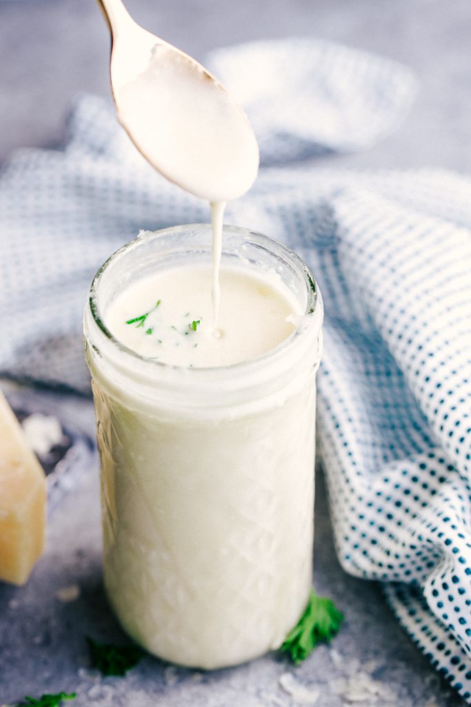 This easy FETTUCCINE ALFREDO recipe is simply delicious. Cheesy, creamy and made from scratch, this sauce is the perfect comfort food made at home. alfredo sauce in a a glass jar with a spoonful above it