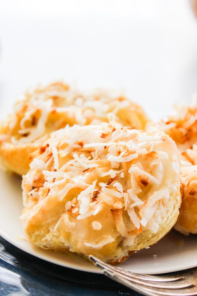COCONUT KNOTS otherwise known as Coco Knots are deliciously sweet puff pastry that's ready in 30 minutes. You're just a few ingredients from eating the best pastry you've ever had. Coconut Knots on a white plate with a fork