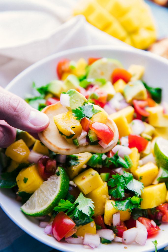 Mango salsa on a bite sized cracker over a bowl of the mango salsa