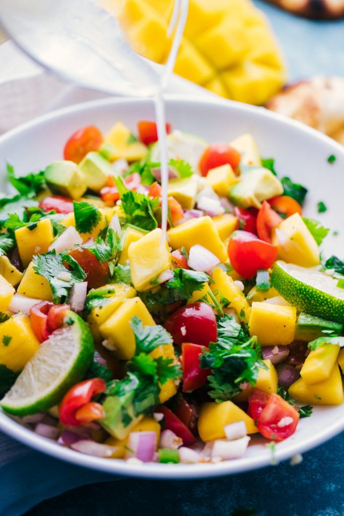 Drizzling lime juice over bowl of mango salsa