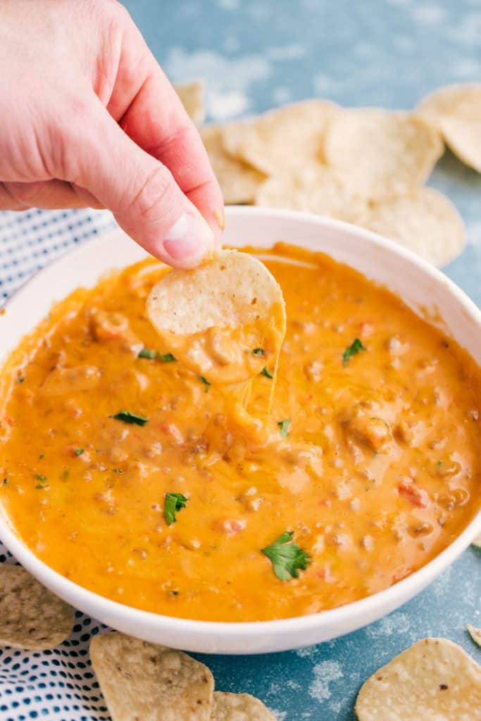 This easy game-day recipe for Sausage Queso Dip is simple to make, only takes minutes to throw together and makes enough to feed a crowd. hand dipping tortilla chip into a bowl of sausage queso dip