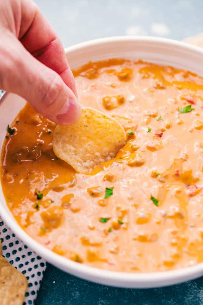 sausage queso with chip being dipped in it with hand