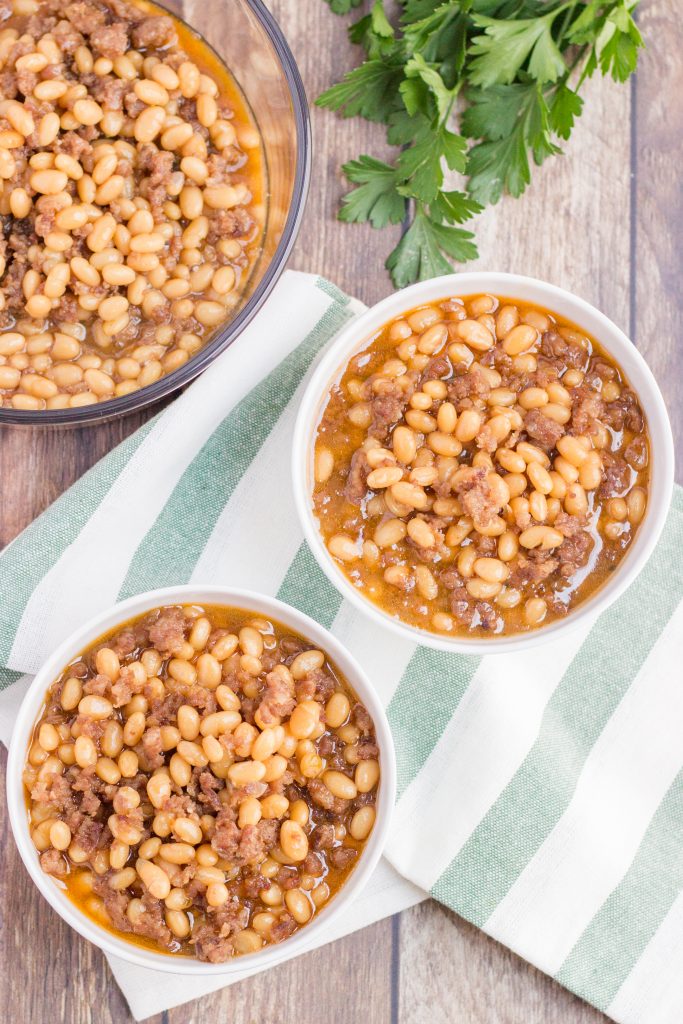 2 white bowls full of navy beans with a glass serving bowl of beans
