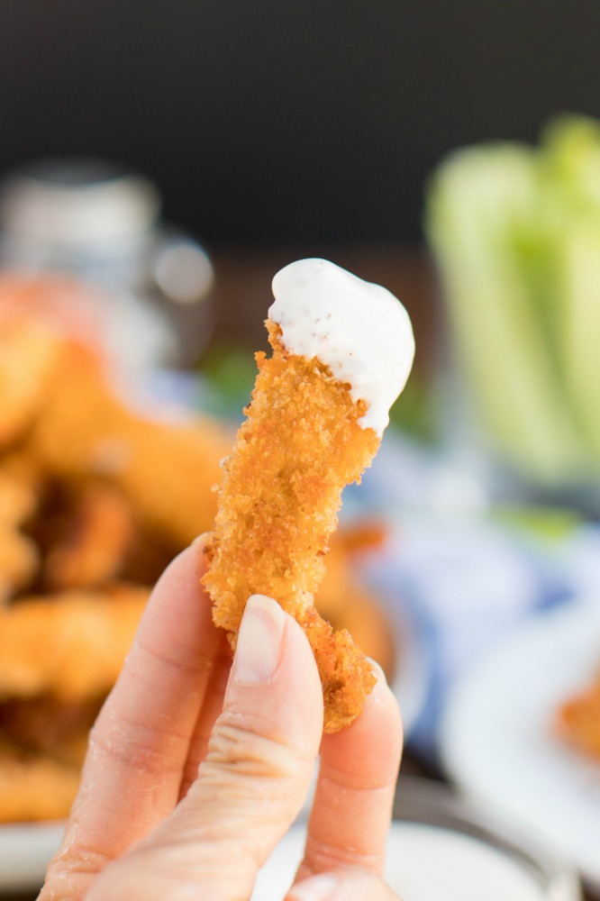Buffalo Pork Tenderloin Fries are thin crispy strips of panko crusted pork, seasoned then dipped in a buffalo sauce-egg mixture and fried. close up of a pork tenderloin fry dipped in ranch