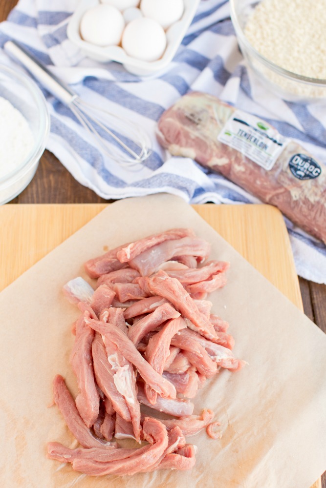 Buffalo Pork Tenderloin Fries are thin crispy strips of panko crusted pork, seasoned then dipped in a buffalo sauce-egg mixture and fried. photo of sliced raw pork tenderloin on a cutting board, with ingredients in background