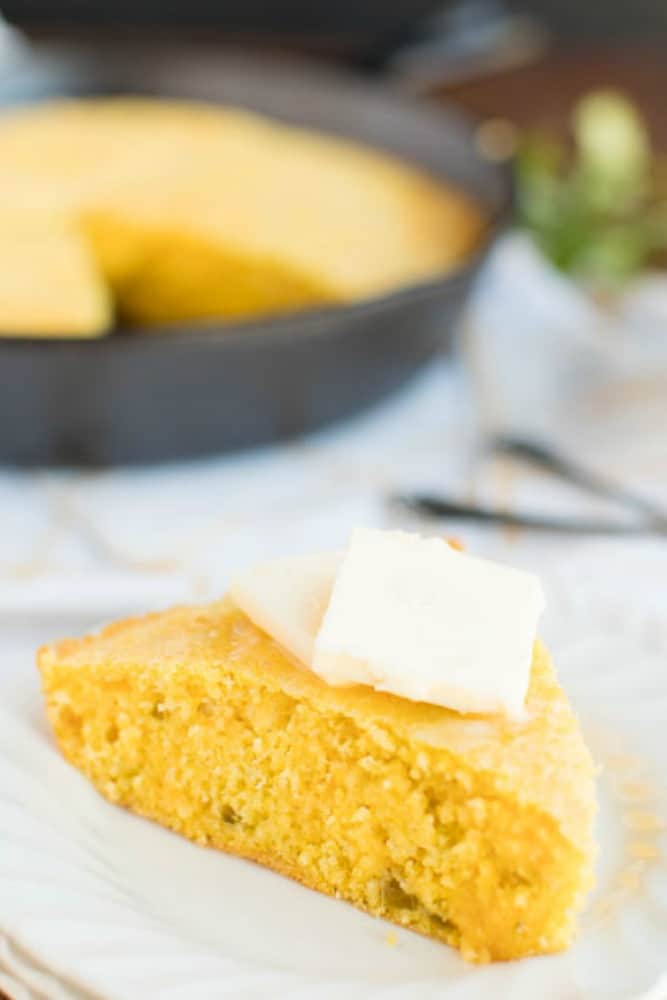 You're going to love this Skillet Cornbread Recipe that's slightly sweet & savory, with a crunchy, buttery crust, from baking it in a cast iron skillet. cornbread slice on a plate with butter on top. skillet in background