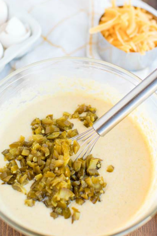 You're going to love this Skillet Cornbread Recipe that's slightly sweet & savory, with a crunchy, buttery crust, from baking it in a cast iron skillet. cornbread batter in a glass bowl with jalapenos being stirred in with a metal whisk