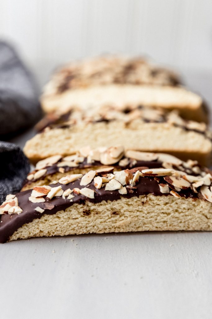 close up of biscotti dipped in chocolate and almonds on a counter, laid in a row