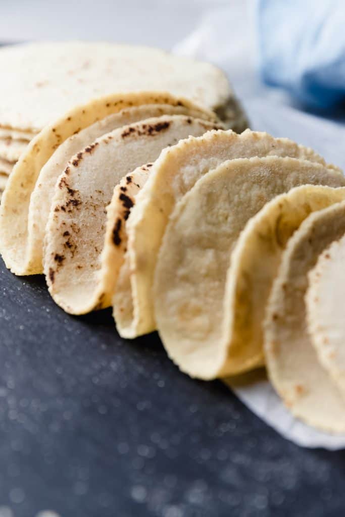 row of folded homemade corn tortillas next to a stack of tortillas