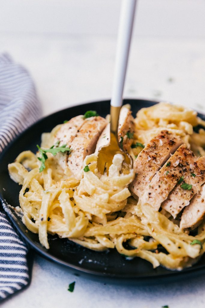 This recipe for Skinny Alfredo Sauce is insanely delicious, creamy & lightened up, you will love how flavorful this sauce is with less the calories. photo of pasta with Skinny Alfredo Sauce on a plate with a fork twisting some noodles, topped with sliced chicken