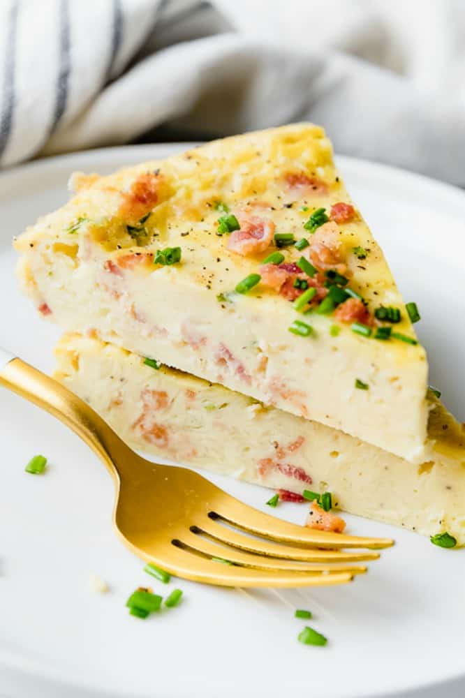 photo of two slices of bacon chive crustless quiche stacked on a white plate with a gold fork
