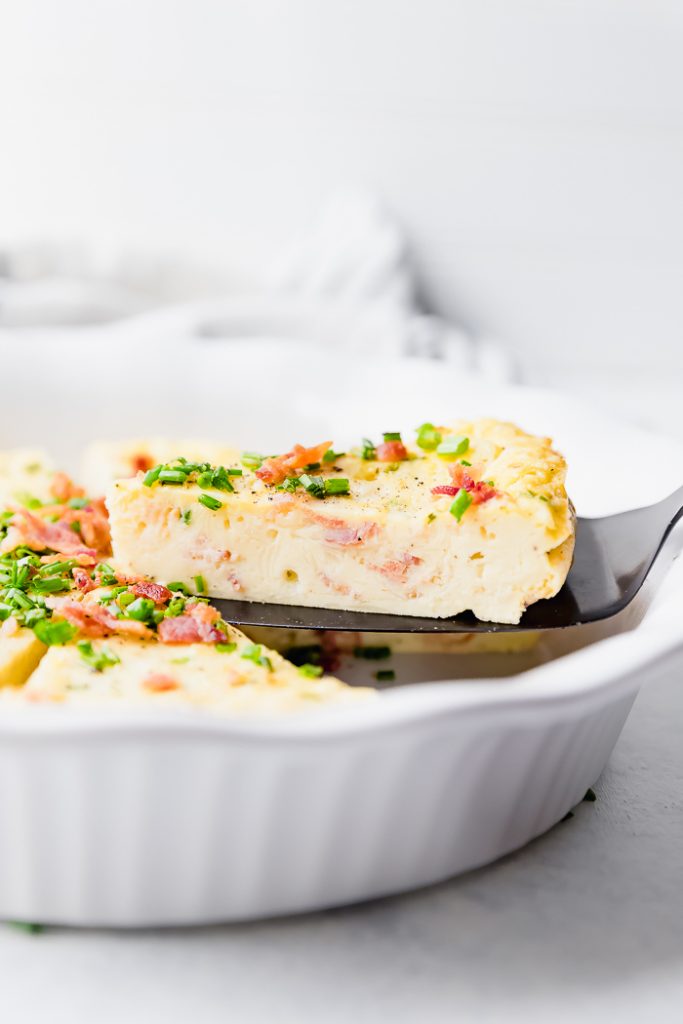 photo of a slice of Bacon Chive Crustless Quiche being lifted from the white pie pan