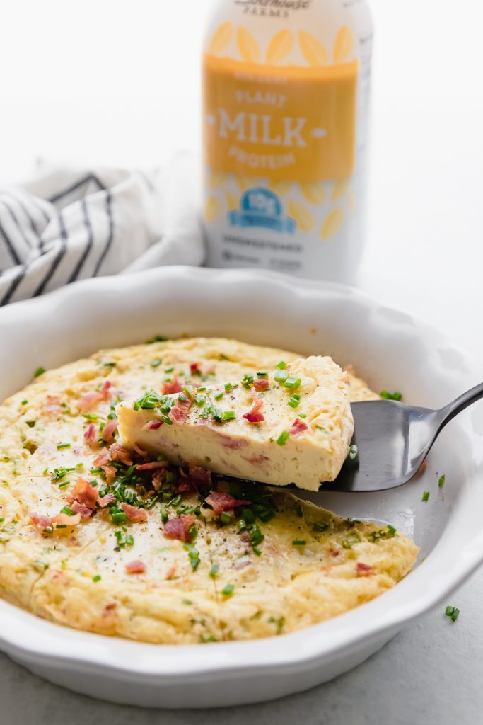 photo of Bacon Chive Crustless Quiche slice being lifted out of pie pan, with plant protein milk bottle in background