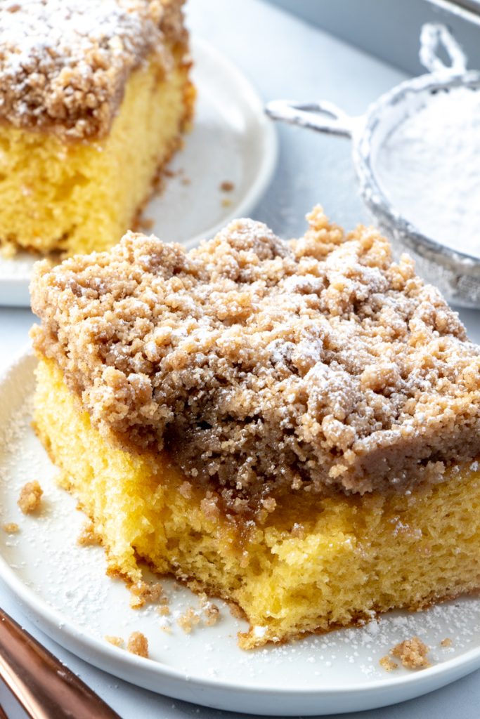 Cinnamon Streusel Coffee Cake - A light & fluffy golden cake topped with a classic cinnamon, brown sugar streusel topping. photo of Cinnamon Streusel Coffee Cake slice on a white plate with bite taken out
