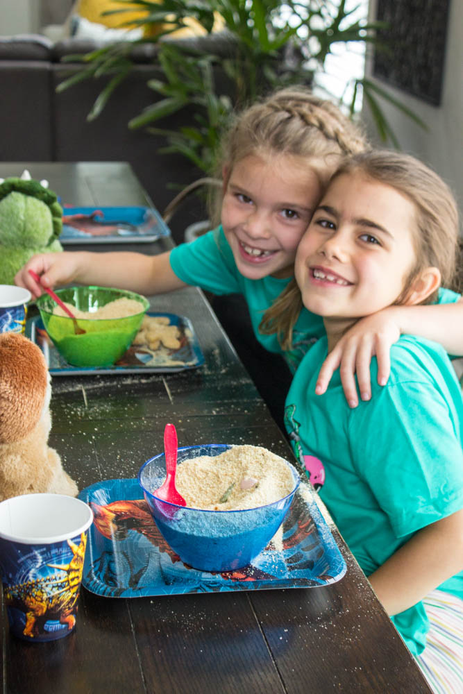 photo of two young girls with arms around each other, sitting at a table with dino dig bowls in front of them
