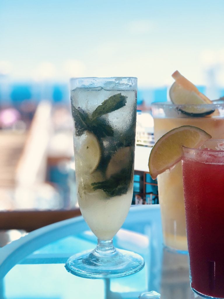 Photo of virgin mojito and other drinks with lime slices on a glass table on cruise deck