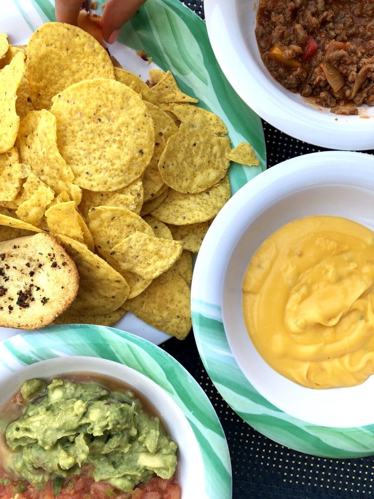 overhead photo of tortilla chips with queso dip, salsa, and guacamole