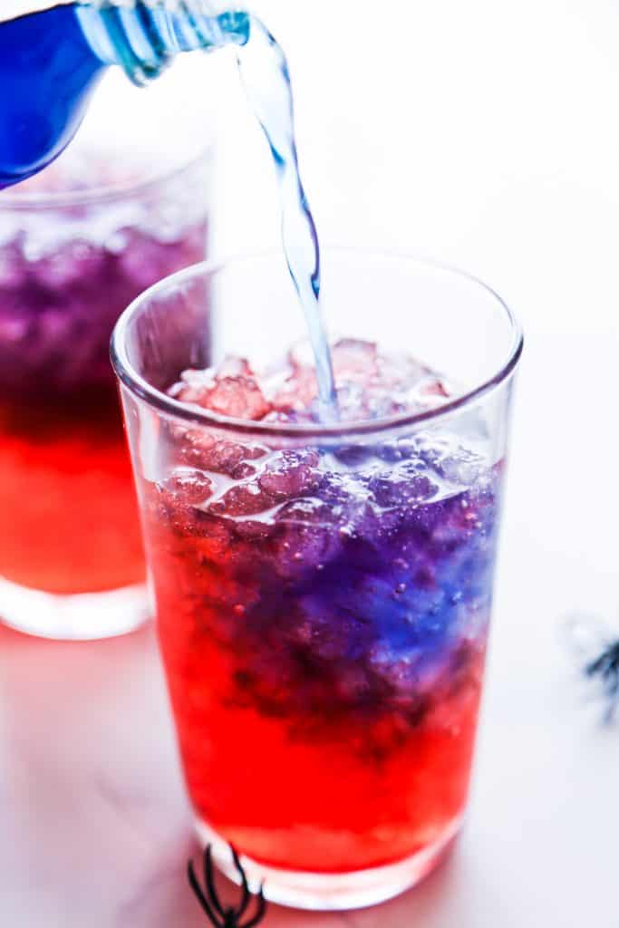 Blue gatorade being poured into a cup with red soda and ice
