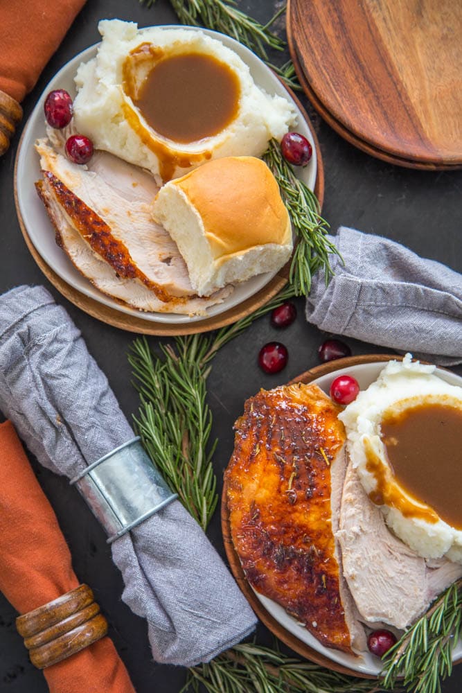 two plates with turkey, mashed potatoes, gravy, and rolls.