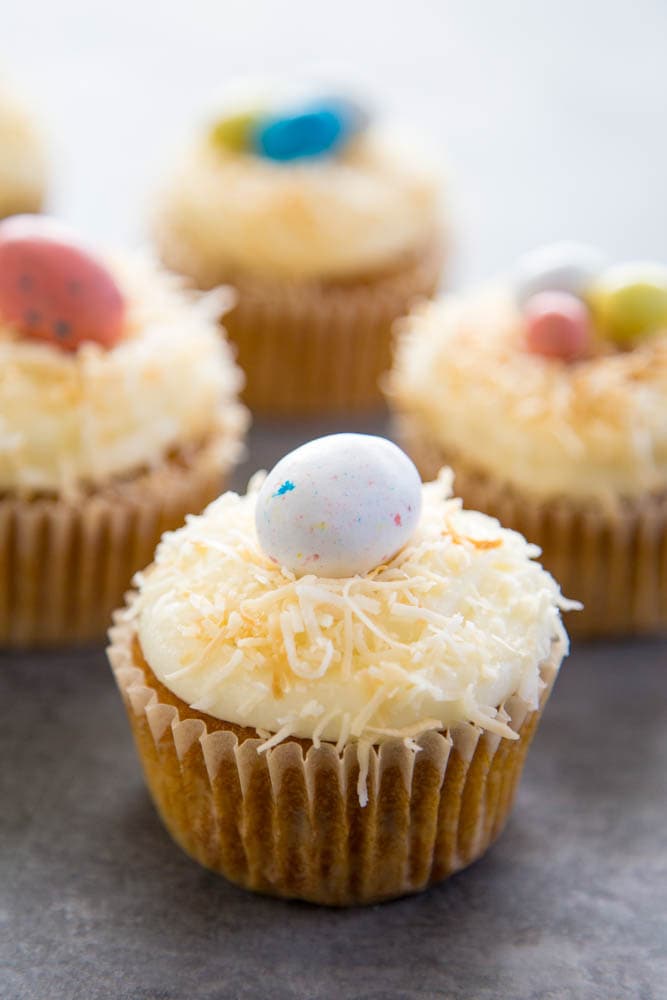 carrot cake cupcakes topped with frosting, coconut, and a candy egg.