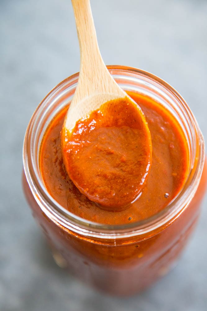 a wooden spoon dipped into a jar of enchilada sauce.