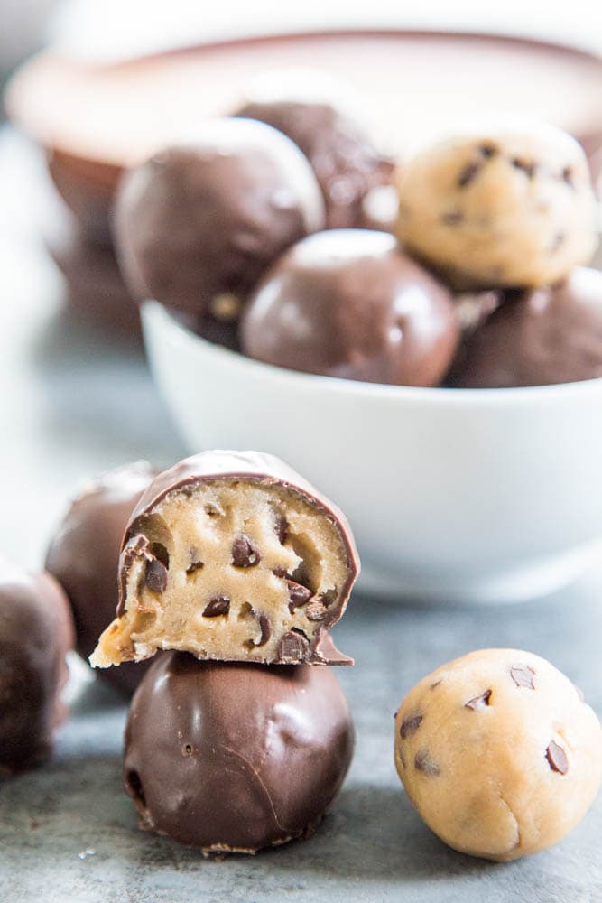 chocolate coated cookie dough bites with a bowl in a background.