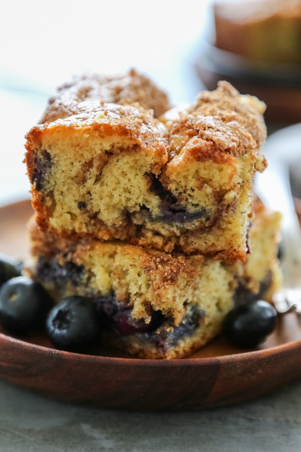 This Simple Blueberry Coffee Cake is a perfect start to your day. With blueberry Greek yogurt, this coffee cake is rich and deliciously moist. Two slices of coffee cake stacked on a plate with blueberries.