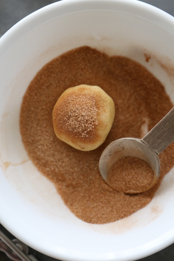cookie dough ball being rolled in cinnamon sugar.
