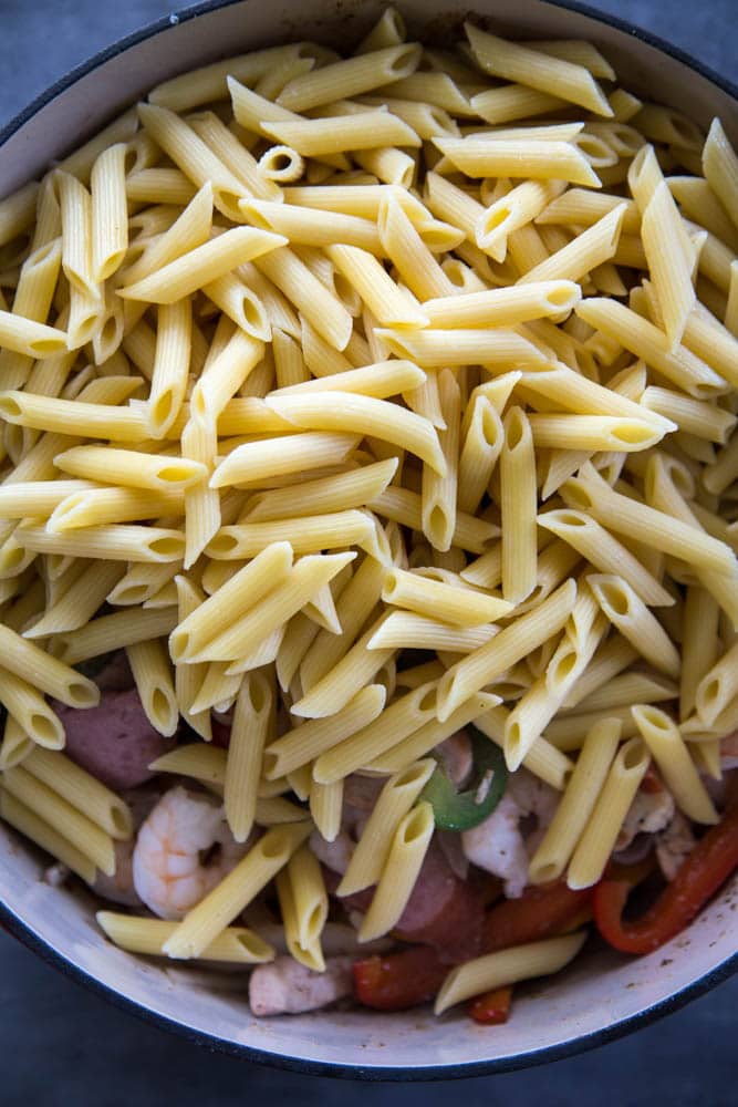 the penne pasta being added to the pan.