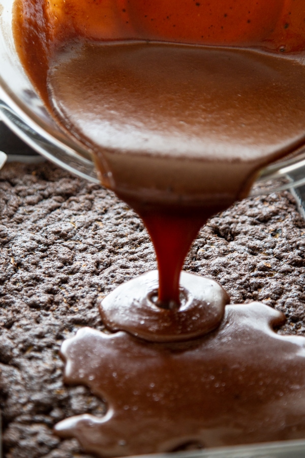 the frosting being poured over the brownies.