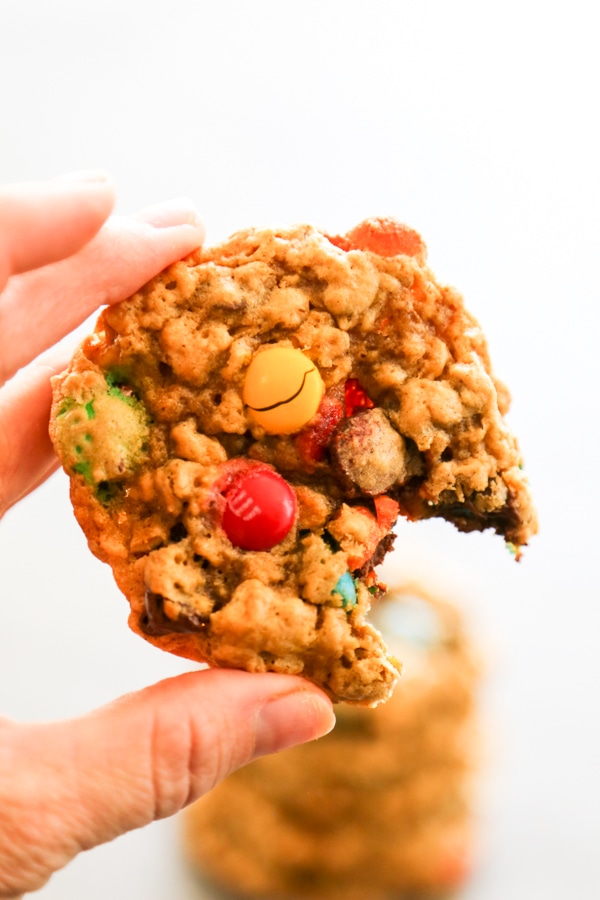 a hand holding one Pumpkin Monster Cookie with a bite taken out of it.