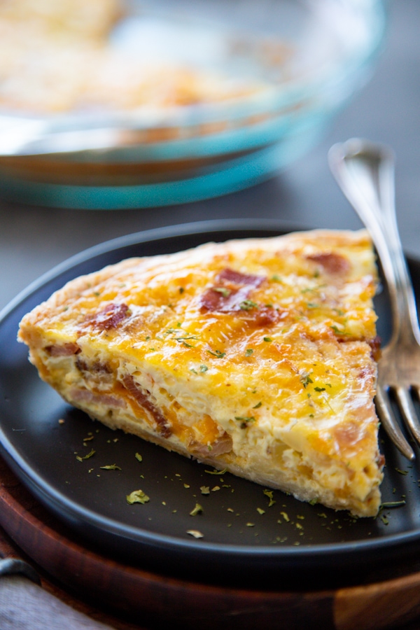 a slice of bacon quiche on a black plate.