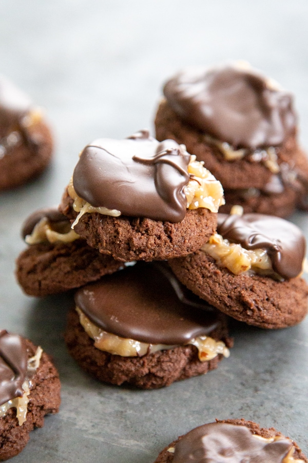 These Mini German Chocolate Thumbprint Cookies are fudgey-brownie like cookies topped with a chocolate drizzle, toasted coconut, and chopped pecans. a pile of thumbprint cookies.