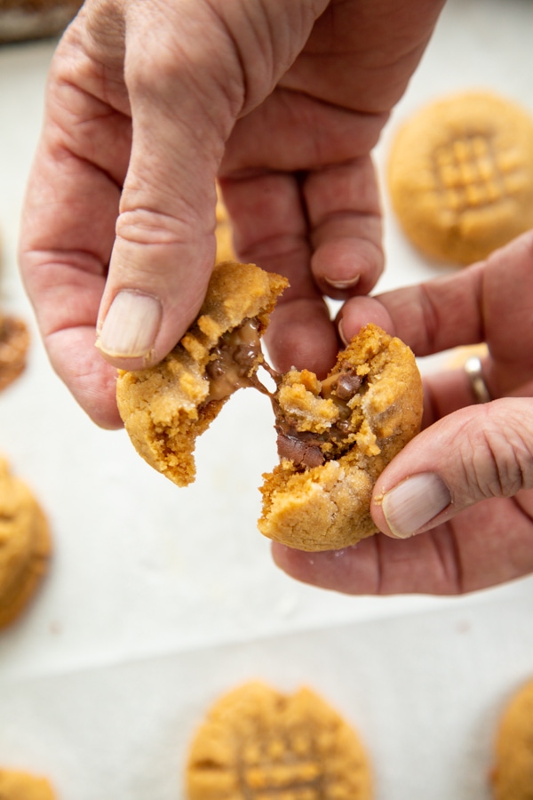 two hands pulling apart a peanut butter cookie with a caramel chocolate center