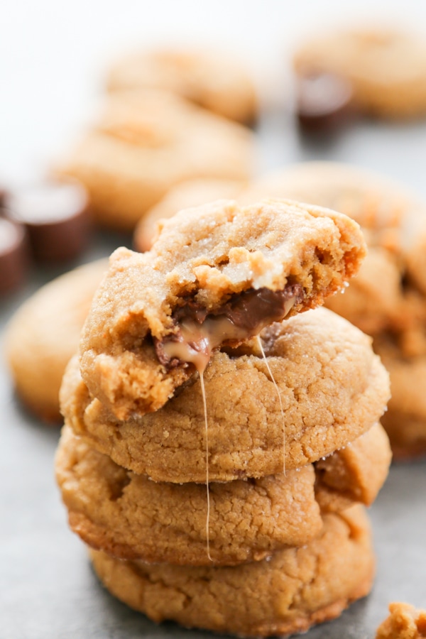 Rolo Stuffed Peanut Butter Cookies are soft and chewy peanut butter cookies with a delicious, melt in your mouth chocolate & caramel center. a stack of cookies with the top one oozing chocolate and caramel.