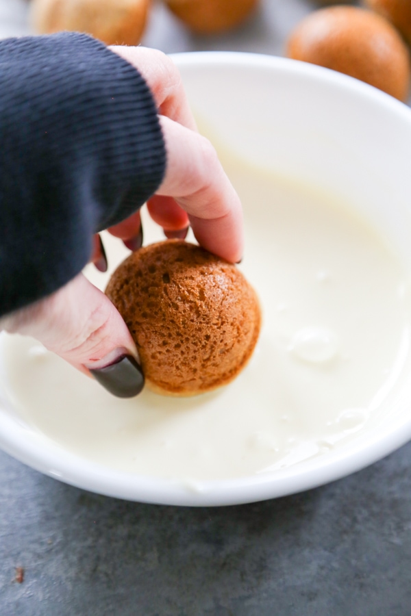 a carrot cake donut hole being dipped in icing.