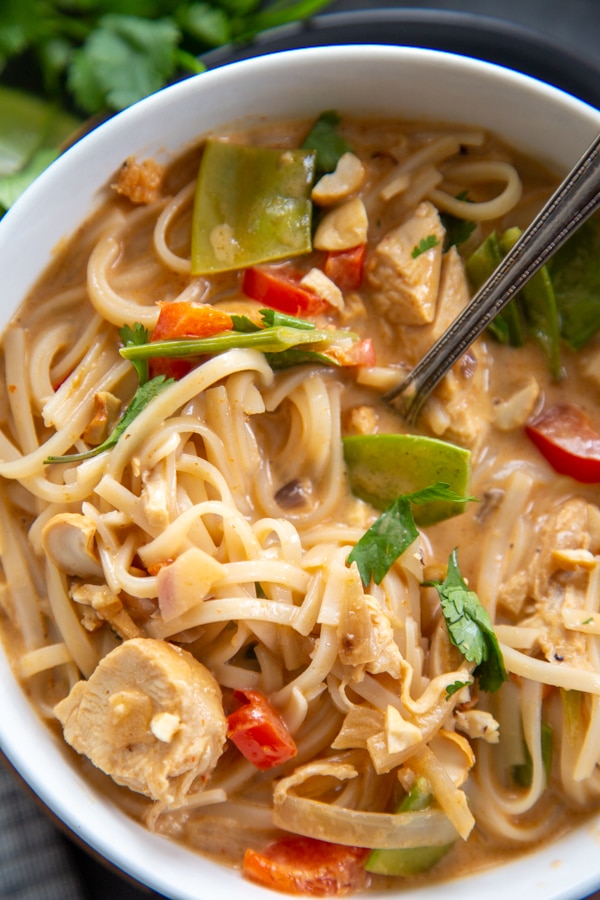 30 Minute Thai Chicken Soup is easy to make but has all the traditional flavors of a classic Thai soup: coconut, curry, cilantro, and fresh lime. close up shot of the soup in a bowl with a spoon.