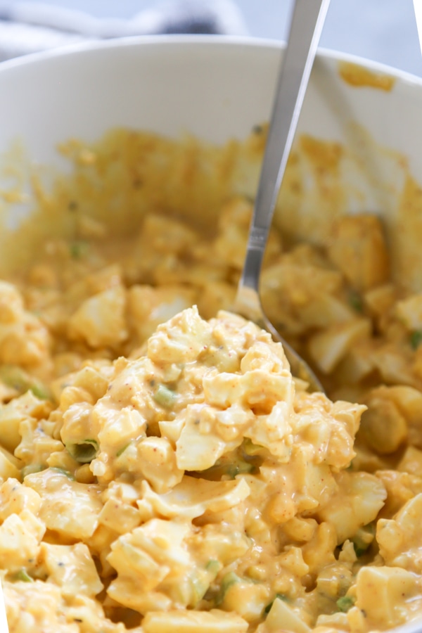 a scoop of egg salad being lifted out of a bowl.