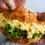 hands holding an egg salad sandwich.