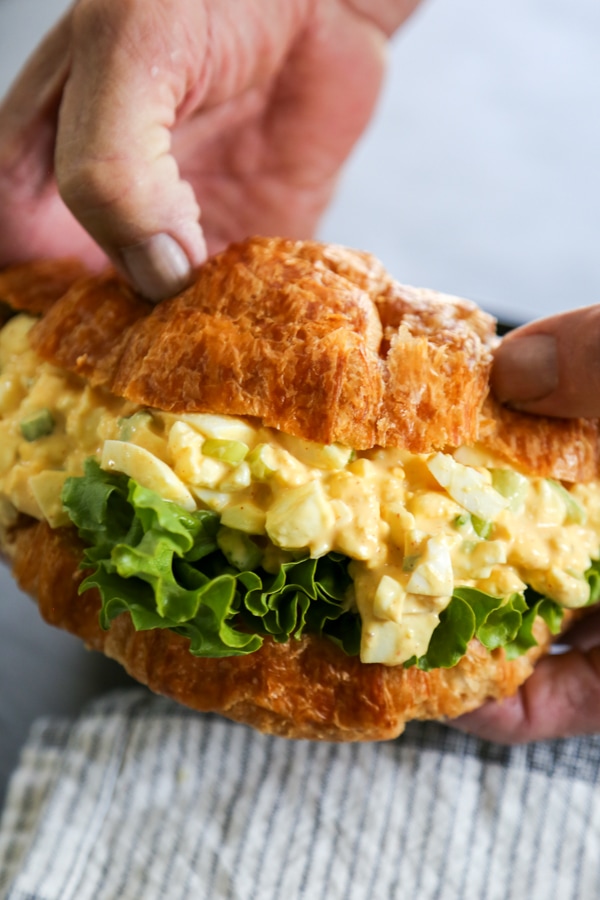 hands holding an egg salad sandwich.