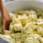 a bowl of potato salad with a wooden spoon.