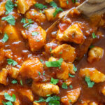 sweet and spicy chicken in skillet with wooden spoon topped with cilantro