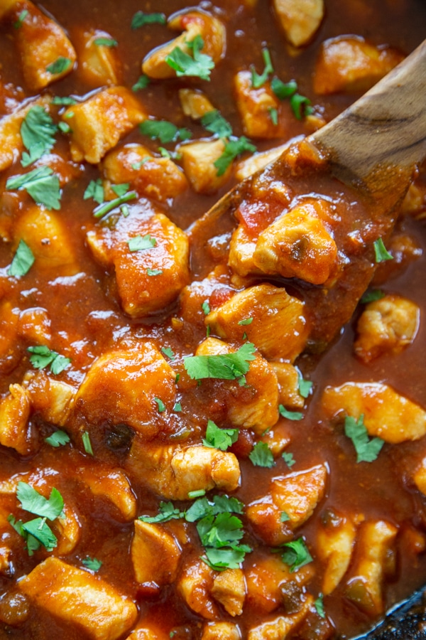 sweet and spicy chicken in skillet with wooden spoon topped with cilantro